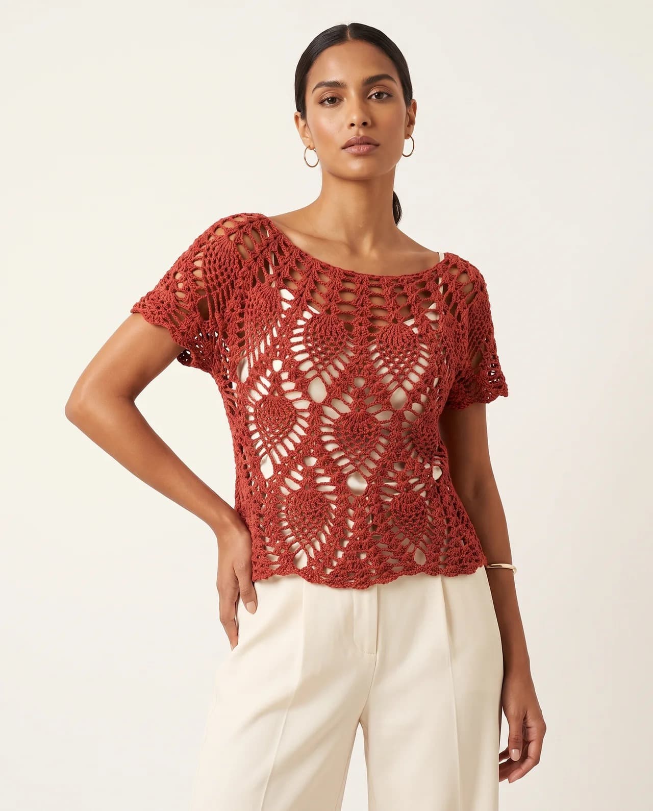 Model in a short-sleeved coral open-work crochet top with cream trousers