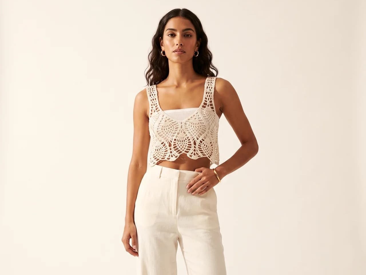 Model in a cream crochet cropped top with white wide-leg trousers