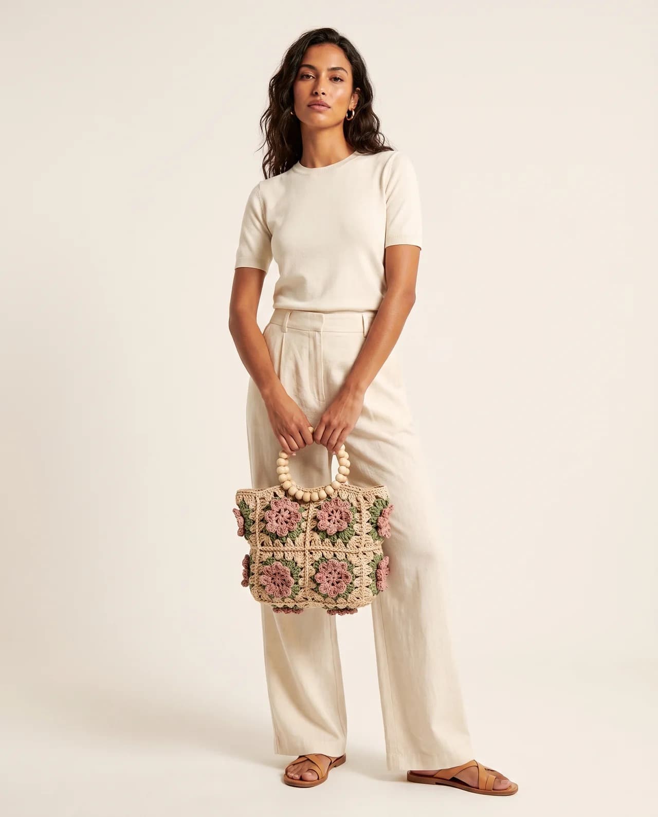 A floral granny-square crochet bag trimmed with pompoms, carried at the hip