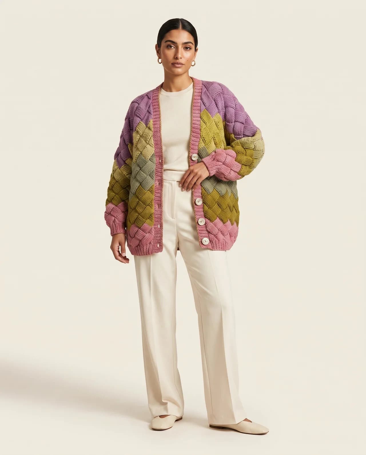 Model in a patchwork crochet cardigan in pink, violet and olive, over cream trousers
