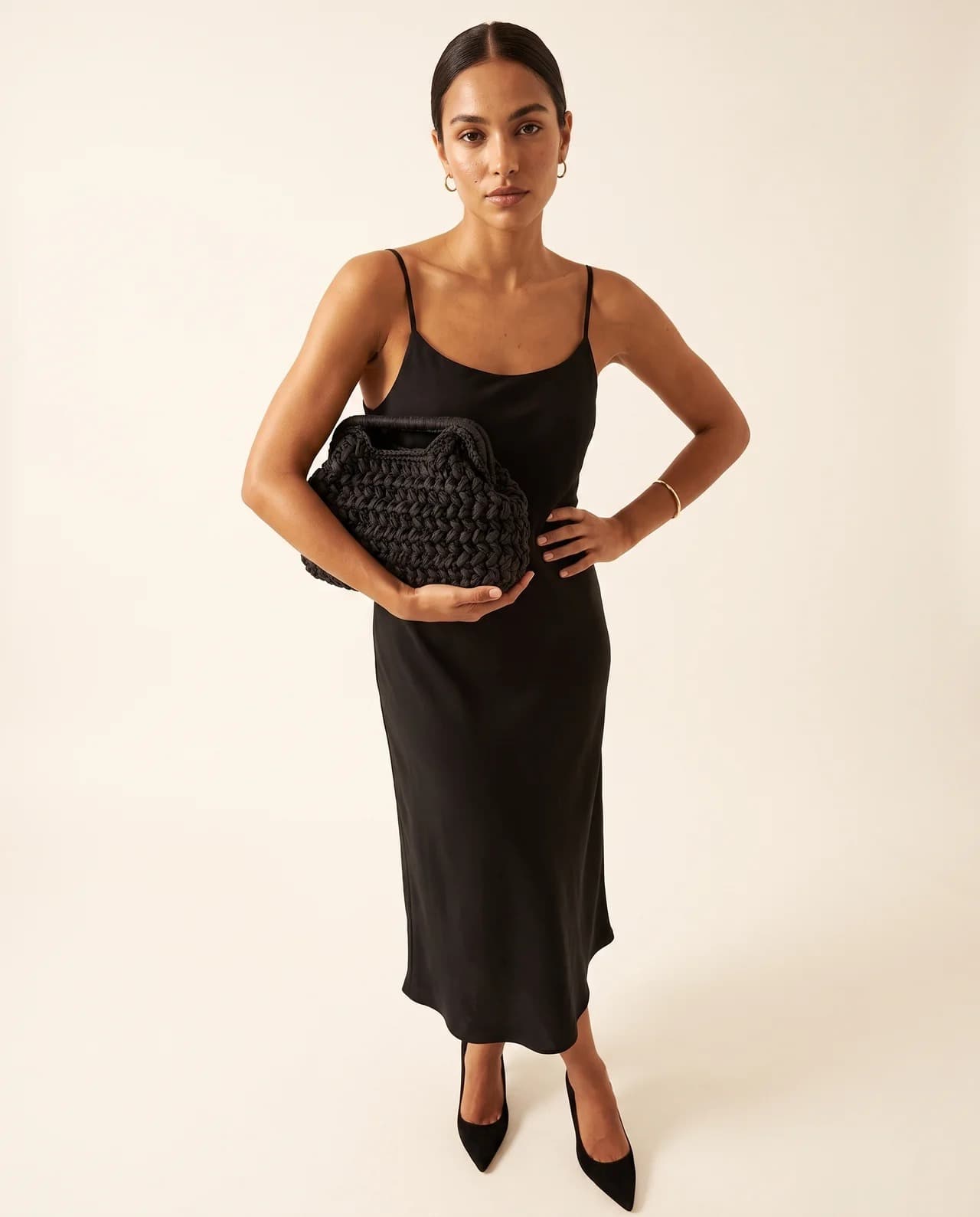 Model in a black slip dress holding the Perla, a beaded evening bag with a structured body