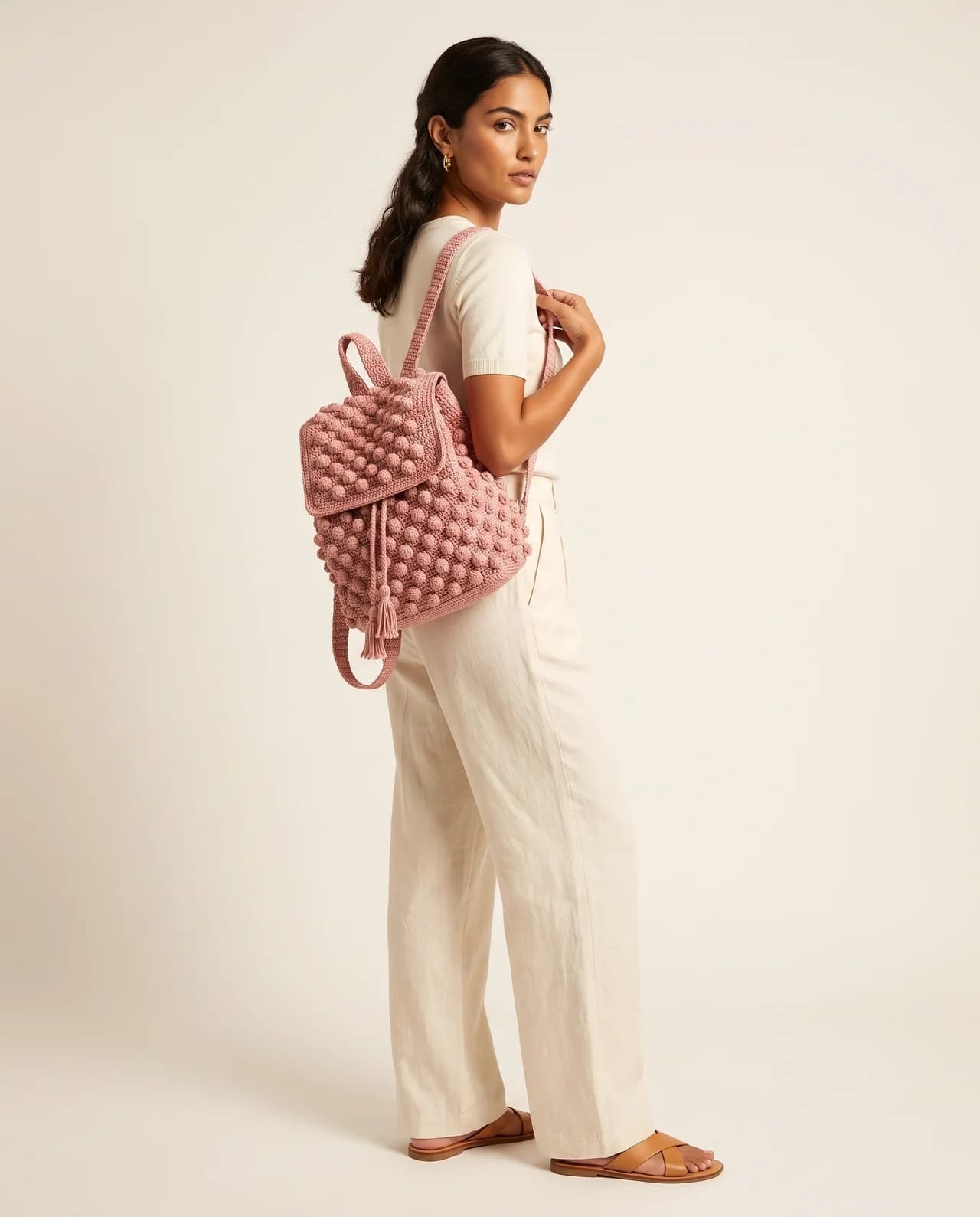 Model in cream linen wearing the Quadro Backpack, a soft pink checked crochet backpack
