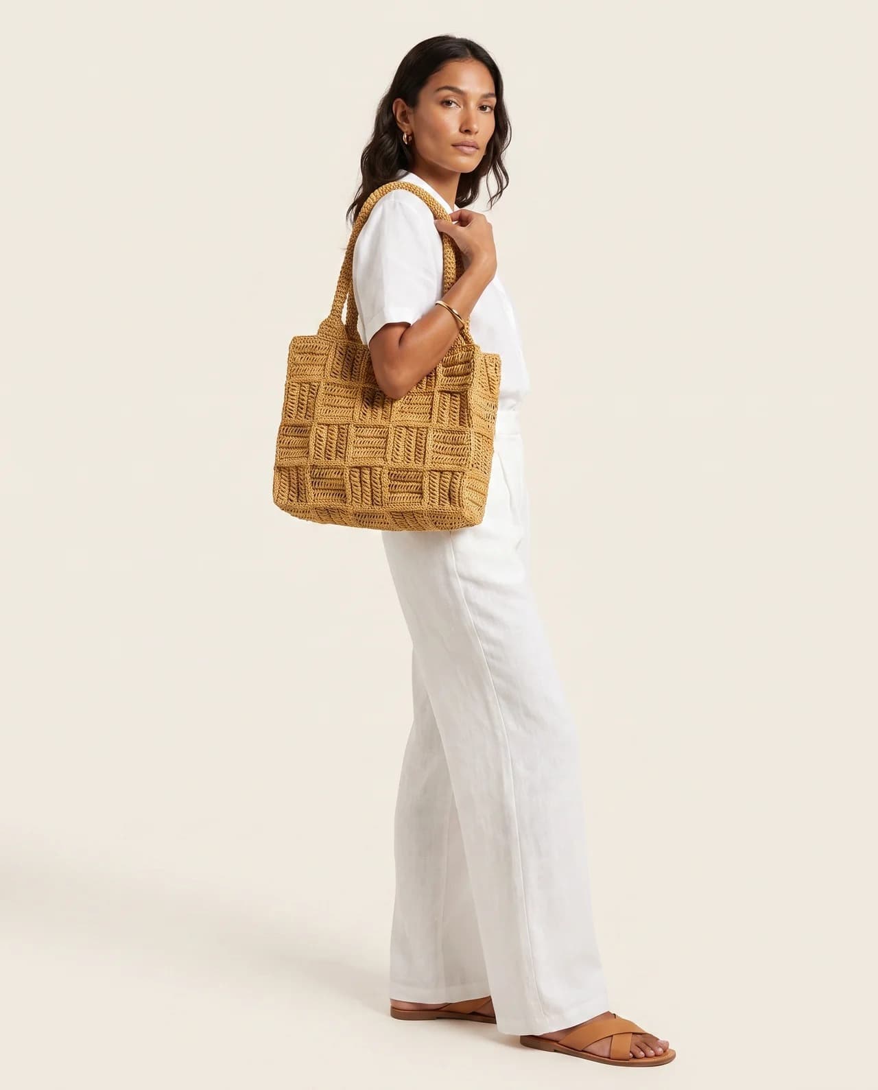 Model in white linen carrying the Rafia Tote, a woven natural-fibre bag with a raised pattern