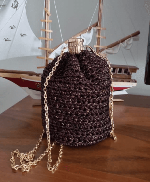 A burgundy crochet drawstring pouch with a gold chain strap